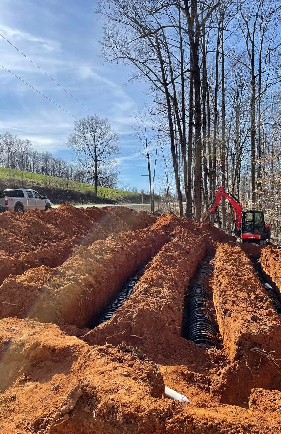 A mini-excavator shaping parallel chamber trenches at an EMS install