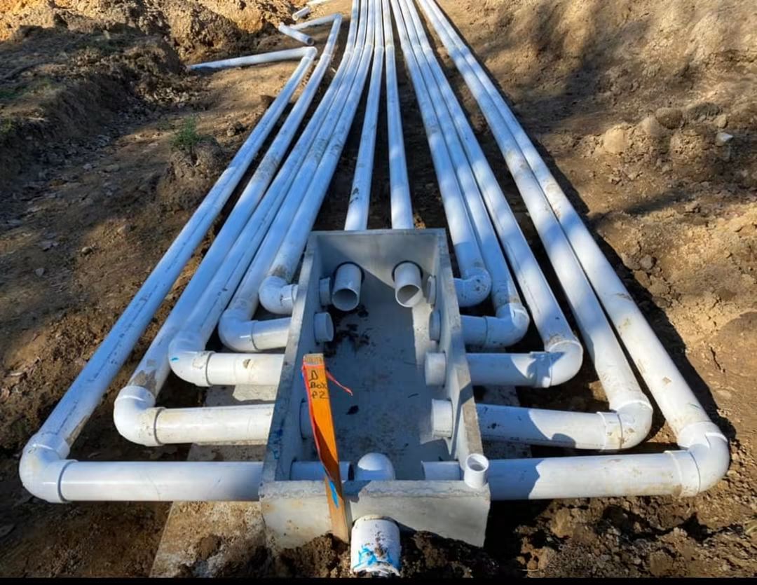 Concrete distribution box with PVC lateral lines fanning out toward the trenches at an EMS drain field installation