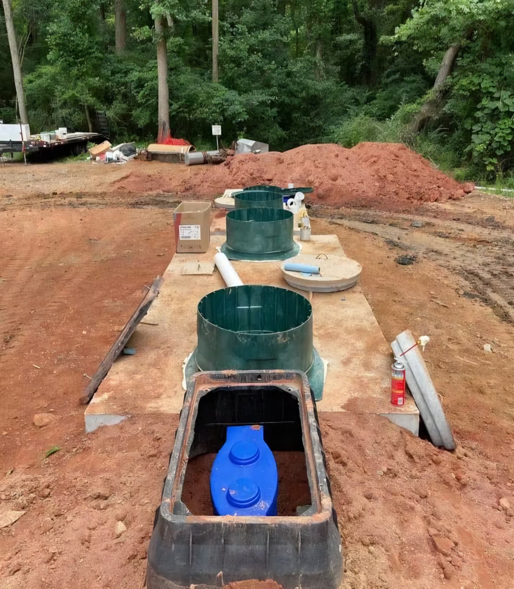 Tank installation with green risers and a blue pump vault in an excavated site