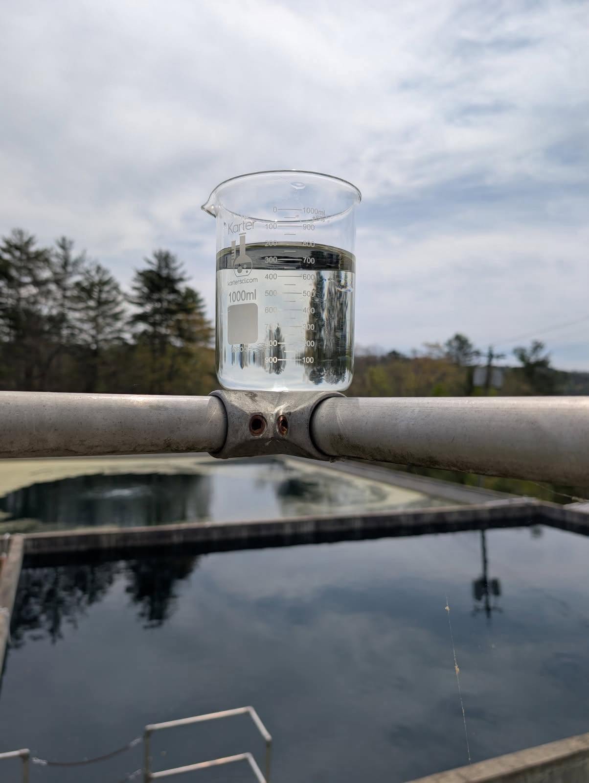 Laboratory beaker with a wastewater sample held at a treatment lagoon