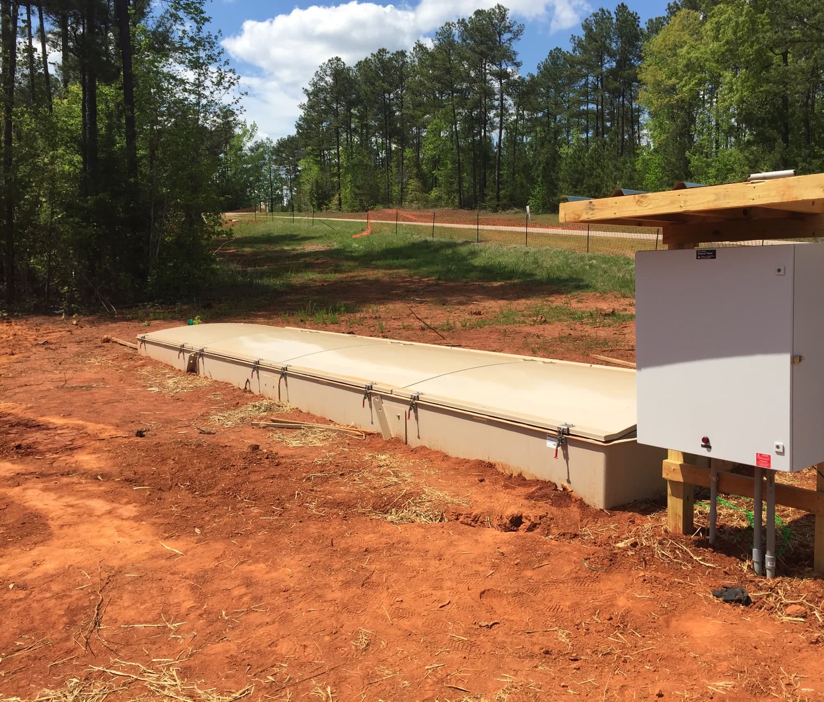 Completed Orenco treatment unit with latched fiberglass covers and a control panel under a wooden canopy, installed in red clay