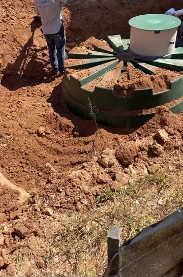 EMS crew lowering a green Orenco treatment tank into the excavation
