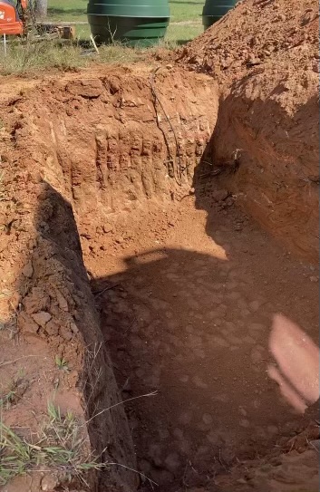 Freshly cut trench with green Orenco tanks staged on the surface above